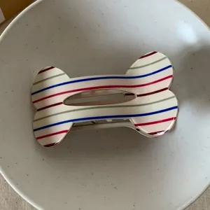 Close-up of a cute bone-shaped striped hair claw clip with colorful patterns in white bowl.