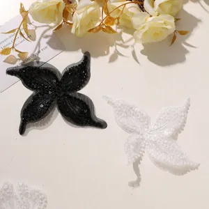 Dettaglio di toppa farfalla fiore in pizzo perlinato ricamato bianco e nero, accessorio DIY.