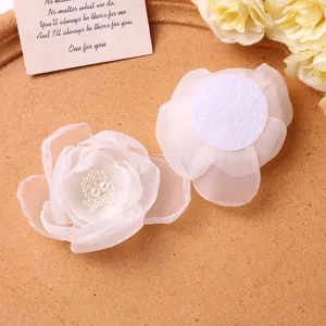 Close up of white mesh fabric flower hair clip detail showing pearl center and felt backing.