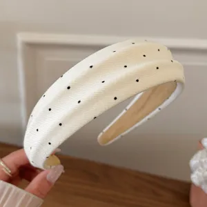 Detailed close-up of a chic white headband featuring a classic black polka dot pattern.