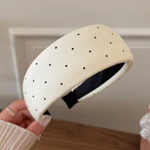 Detailed view of a white wide headband with black polka dots, soft knit fabric texture.