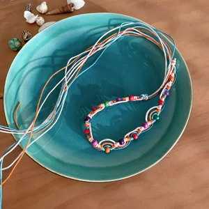 Detail shot of bohemian style colorful braided cord necklace with vibrant beads on ceramic plate.