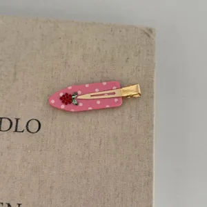 Close-up detail of a pink polka dot hair clip with red rhinestone strawberry and gold clip.