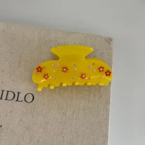Close-up of a yellow resin hair claw clip featuring cute floral and rhinestone decorations.
