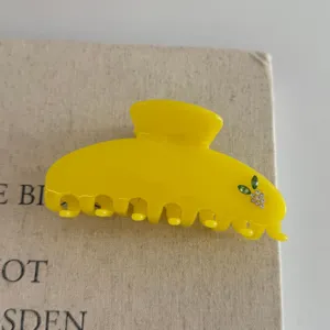 Yellow resin hair claw clip detail shot, featuring sparkling rhinestones and green leaf decor.