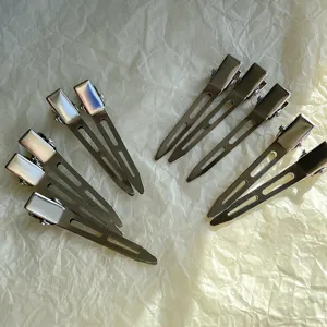 Closeup of metallic duckbill hair clips with hollow design, showing sleek texture and styling details.
