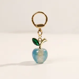 Blue acrylic apple keychain with gold hardware and green crystal leaf charm for bags.