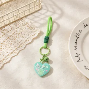 Green heart keychain detail showing cute ghost pendant, woven strap and small bell charm.
