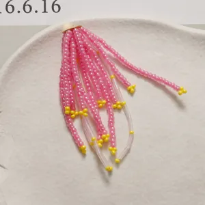 Primo piano dettaglio di materiale artigianale con nappine di perline rosa e gialle fai da te.
