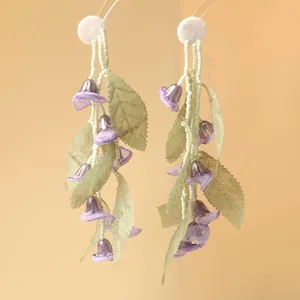 Close-up detail of fairy lily of the valley tassel earrings with beads and green tulle leaves.