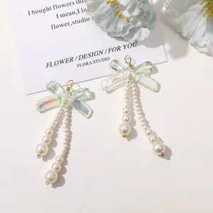 Close-up view of DIY iridescent acrylic bow pendants featuring delicate pearl chains.