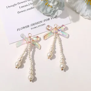 Close-up of iridescent bow pearl drop earrings detail, showcasing shiny resin and beads.
