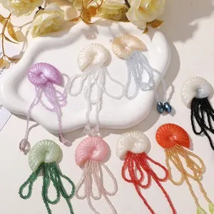 Detailaufnahme einer Harz-Muschel-Brosche mit farbigen Perlenquasten-Hängeaccessoires.
