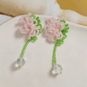 Close-up detail of handmade pink beaded flower earrings with green stem and crystal ball pendant.