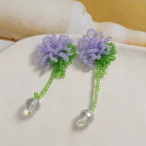 Close-up of handmade beaded flower earrings featuring purple petals and clear crystal pendants.
