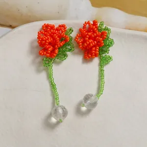 Close-up of handmade beaded orange flower earrings with green stems and clear crystal balls.