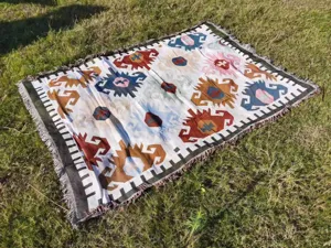Manta de camping bohemia con flecos extendida sobre un campo de hierba verde y fresca