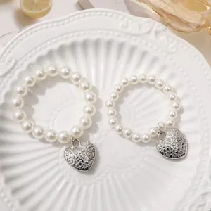 Close-up detail of white faux pearl bracelets featuring shiny silver-tone engraved heart pendants.