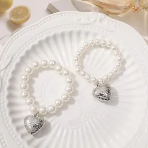 Detailed view of white faux pearl beaded bracelets with vintage carved silver heart pendants for DIY.