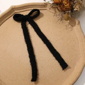 Black fuzzy ribbon bow hair clip detail shot, soft plush material for winter accessories.