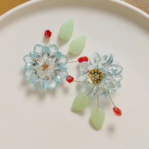 Handmade crystal flower hair accessory detail, blue crystal petals and green leaves craft.