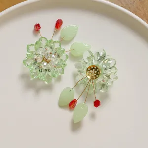 Close-up detail view of handmade crystal beaded flower and green leaf DIY parts with red beads.