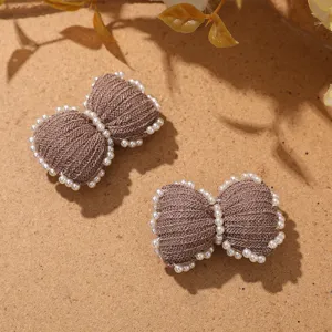Close up detail of brown knit wool bow hair clip decorated with white faux pearls accessories.