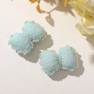 Close-up detail view of light blue knitted wool bow hairpin adorned with white pearls.