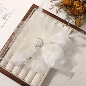 Primer plano de pinza para pelo artesanal de plumas blancas con perlas y pedrería.