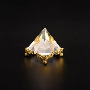 Close-up detail of a transparent crystal pyramid model featuring an ornate gold metal stand.