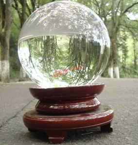 Close-up detail of clear crystal glass ball reflecting forest trees on a traditional wooden stand.