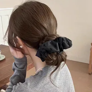 Elegant black hair scrunchie with bow patterns, perfect for styling chic buns and ponytails.