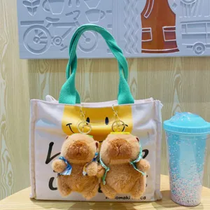 Porte-clés en peluche capybara mignon suspendu à un sac cabas en toile avec design smiley.