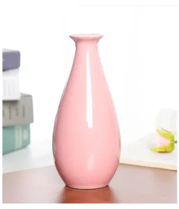 Close-up detail shot of a pink ceramic vase on wooden desk with books and decor flower.