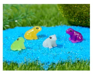 Nahaufnahme von bunten leuchtenden Harzfrosch-Mikrolandschaftsornamenten auf blauem Sand.