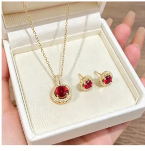 Close-up of red zirconia necklace and earrings set in a white box, shimmering gold pavé details.
