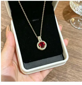 Detail shot of elegant gold-plated red zircon halo pendant necklace in white jewelry box display.