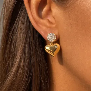 Gold heart earrings detailed close-up shot, sparkling crystal stud and polished metal pendant.