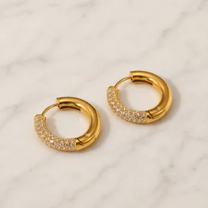 Detalle de elegantes pendientes de aro dorados en acero inoxidable con circonitas brillantes.
