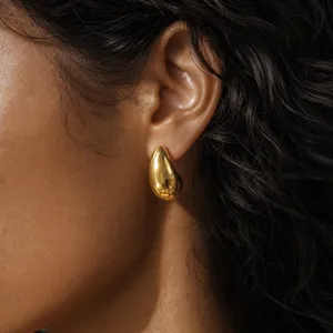 Close-up detail of smooth metallic teardrop stud earrings worn on ear, elegant design.