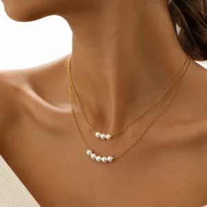 Close-up detailopname van de dubbellaagse goudkleurige ketting met parels om de hals.