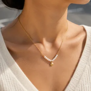 Gold pendant necklace detail showing dainty pearls and seashell charm closeup view.