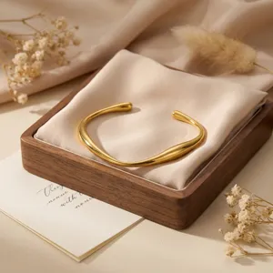 Primer plano detallado de una pulsera rígida abierta dorada minimalista en tela.