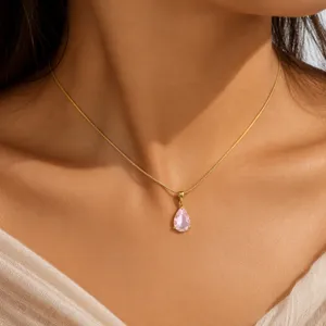 Close-up detail of a delicate gold chain necklace with a sparkling pink pear-shaped zircon pendant.