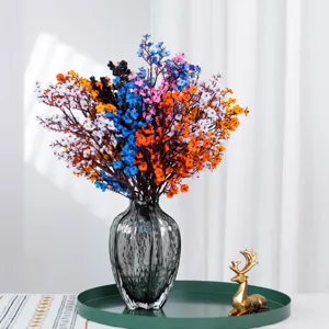 Colorful artificial baby's breath flowers in grey glass vase with tray home decoration.