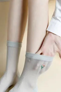Close-up detail of sheer women's socks featuring delicate tulip embroidery and ribbed cuffs.