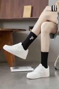 Detail shot of ribbed mid-calf socks with letter embroidery worn by model indoors.