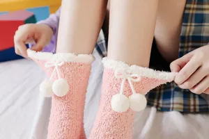 Close-up detail of cute pink fuzzy coral fleece socks featuring fluffy white pom-poms.
