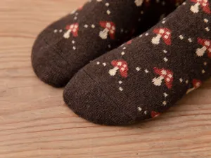 Close-up detail view of thick knit wool socks featuring cute mushroom pattern, soft warm texture.