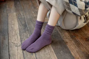 Close-up detail of cozy purple winter knit slouch socks worn on wooden floor background.